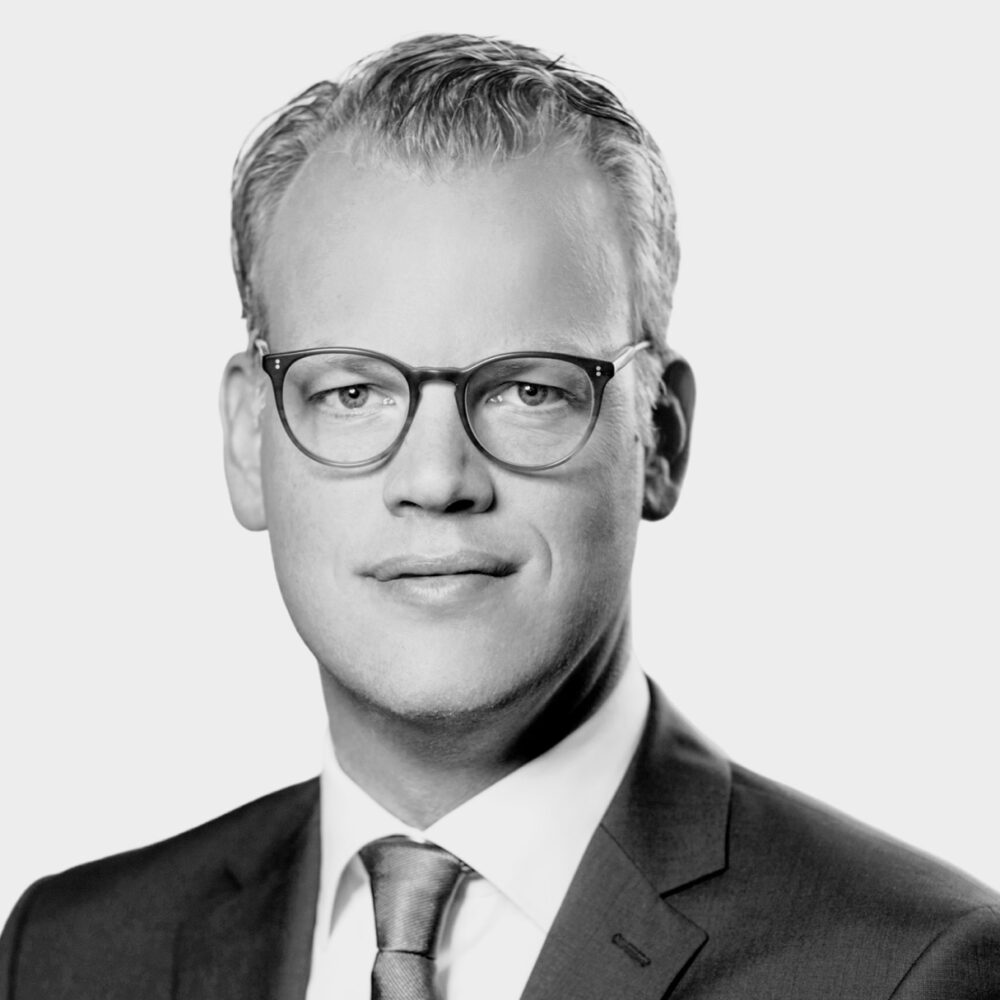 A professional individual in a suit and glasses confidently represents Hoeller Octane Capital in a sophisticated portrait.
